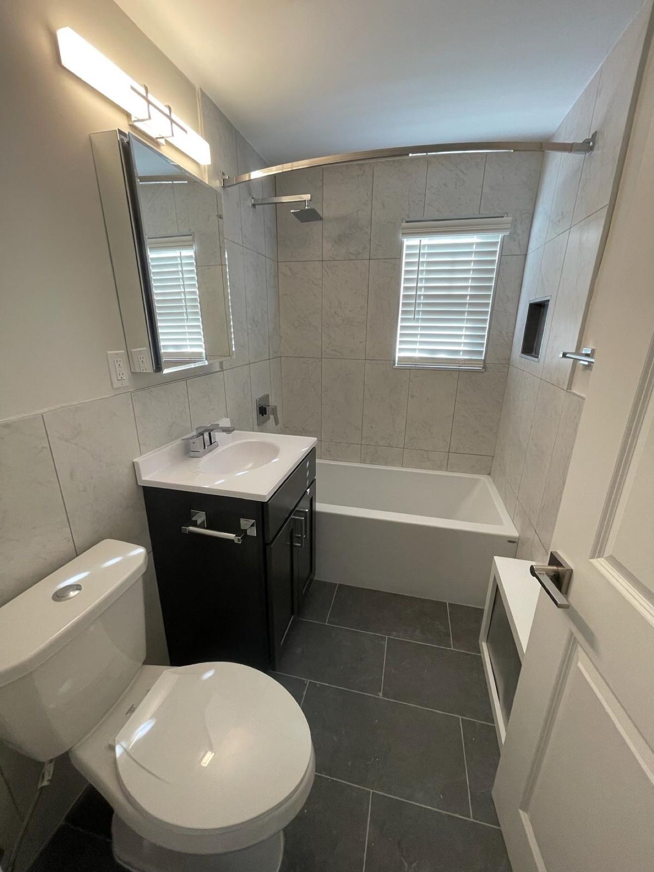 Baño remodelado con losa tipo mármol y tocador negro