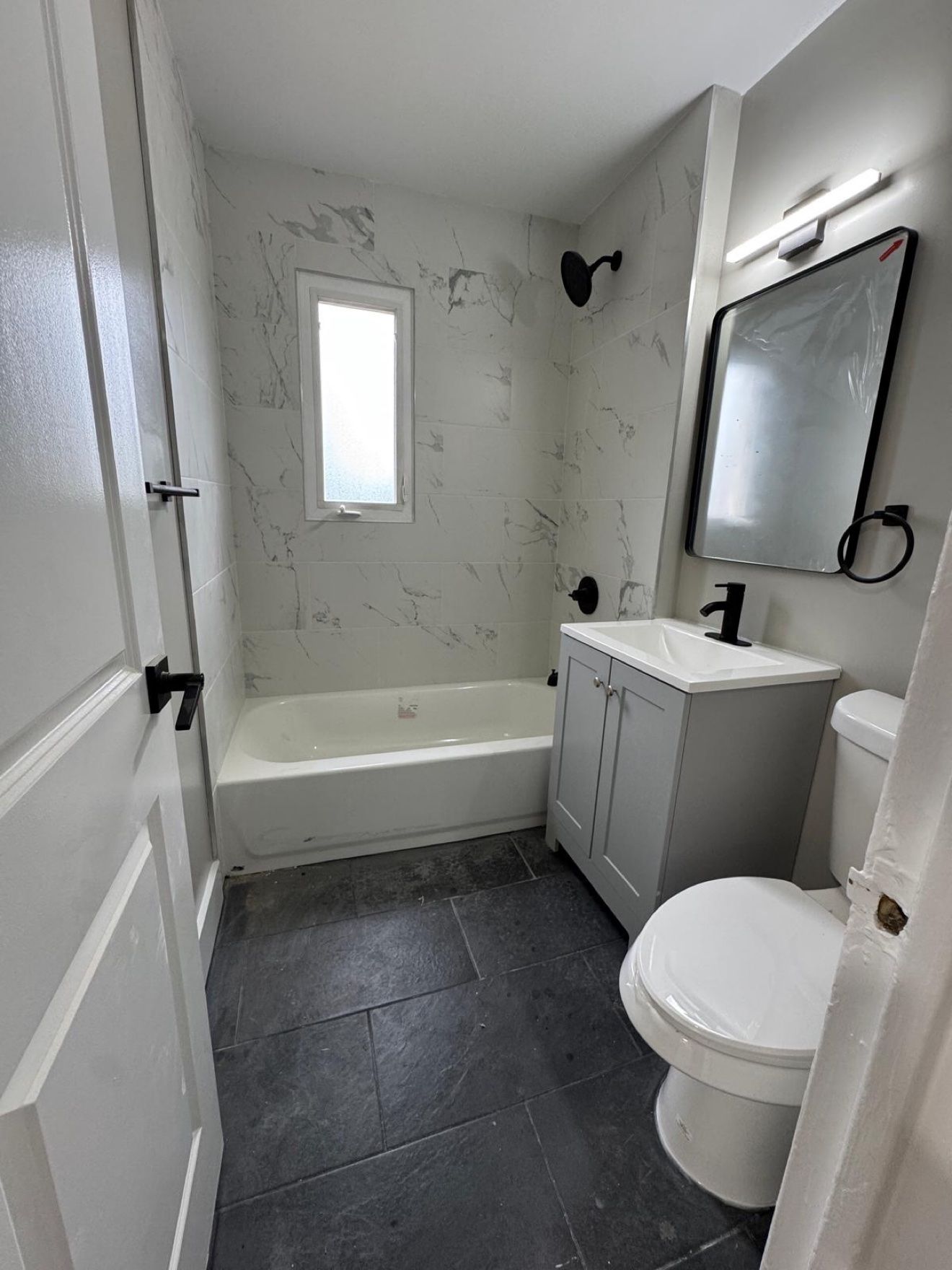 Baño de losa tipo mármol con llaves negras y ventana alta