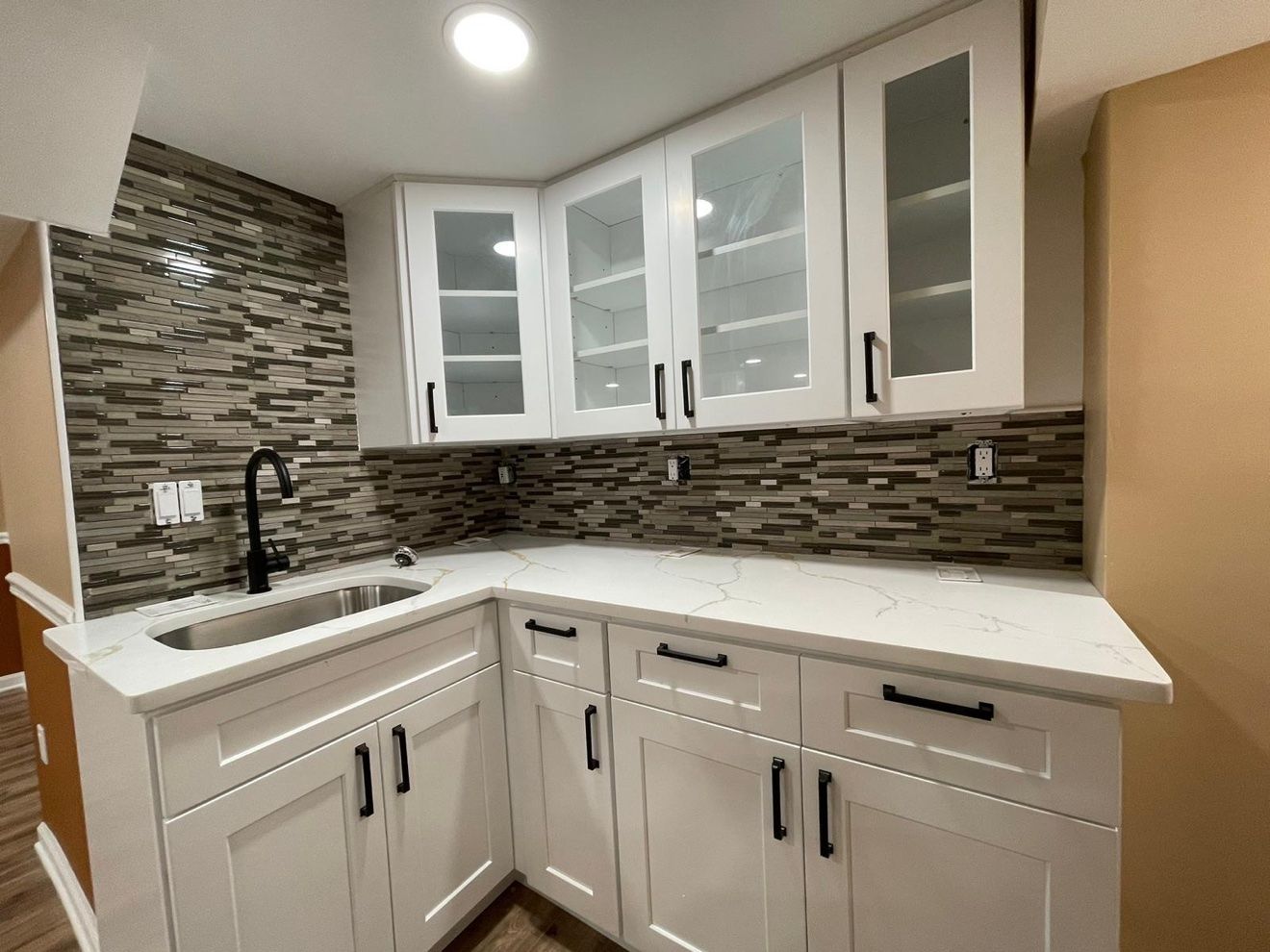 Cocineta con gabinetes blancos de vidrio y backsplash de mosaico